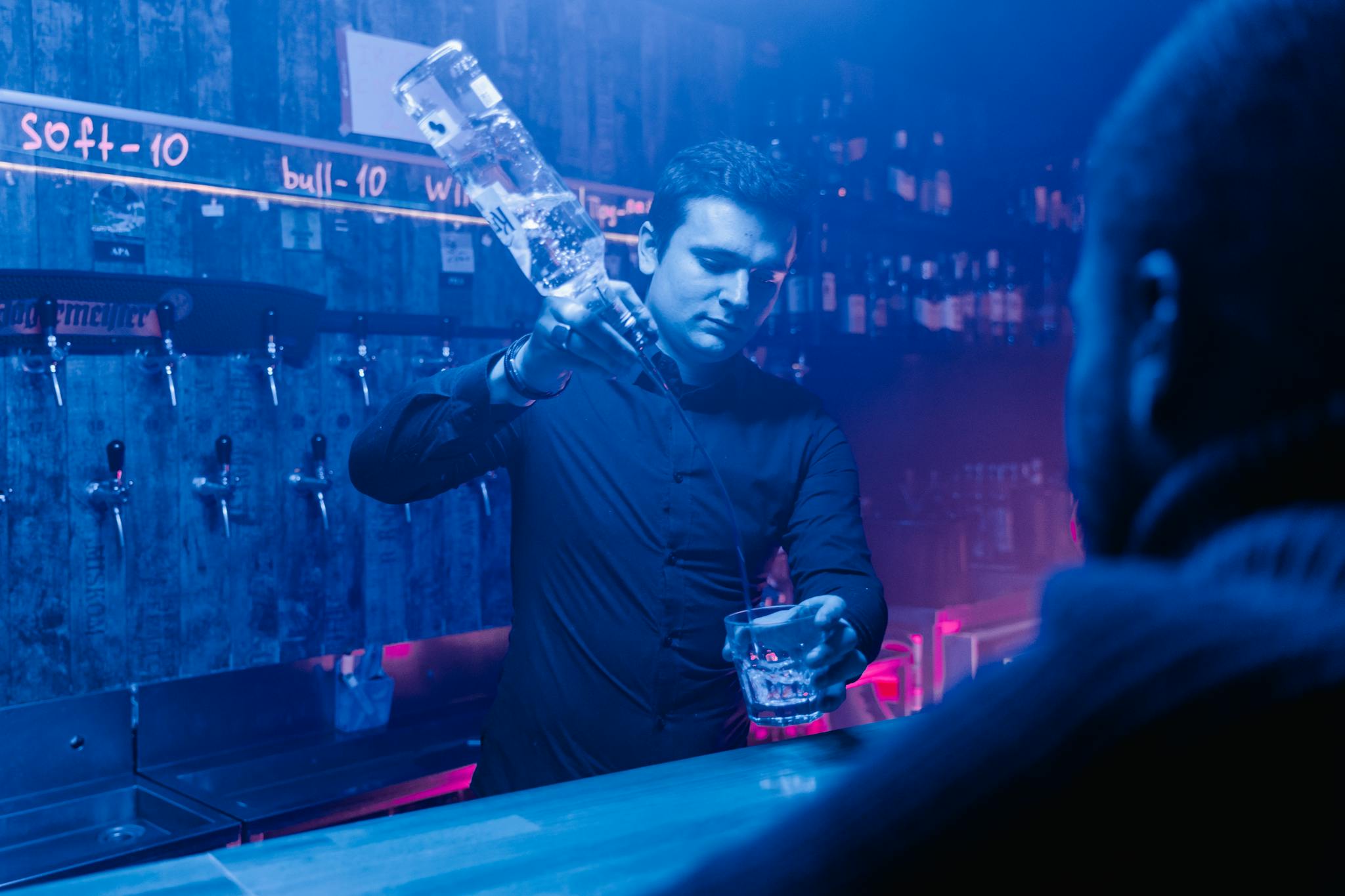 Dynamic nightclub scene with a bartender pouring a drink amid vibrant lighting.