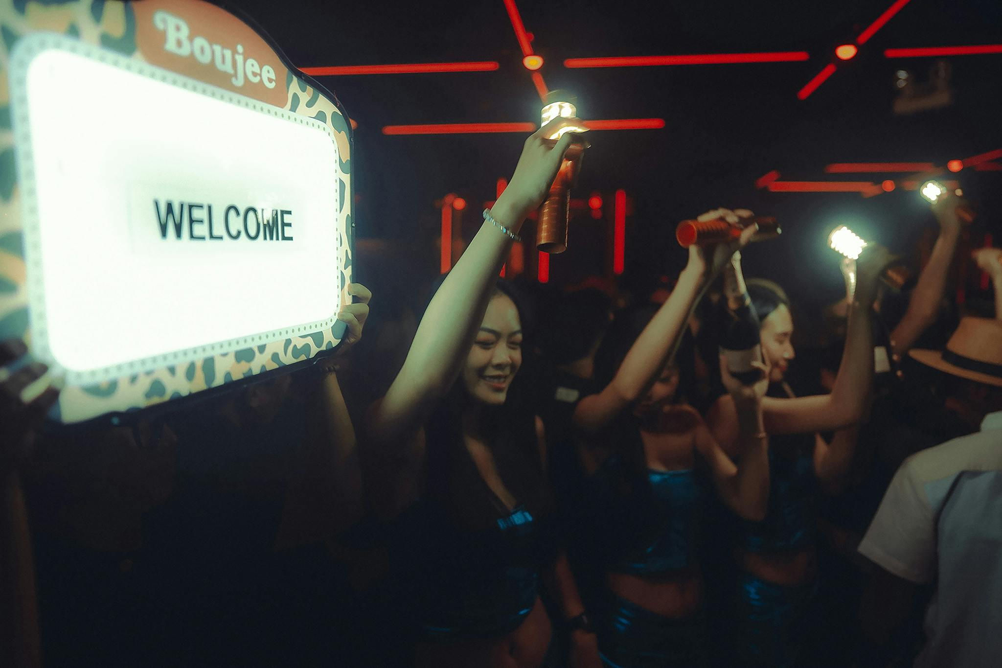 Energetic nightclub atmosphere with people enjoying drinks and dancing under colorful lights.