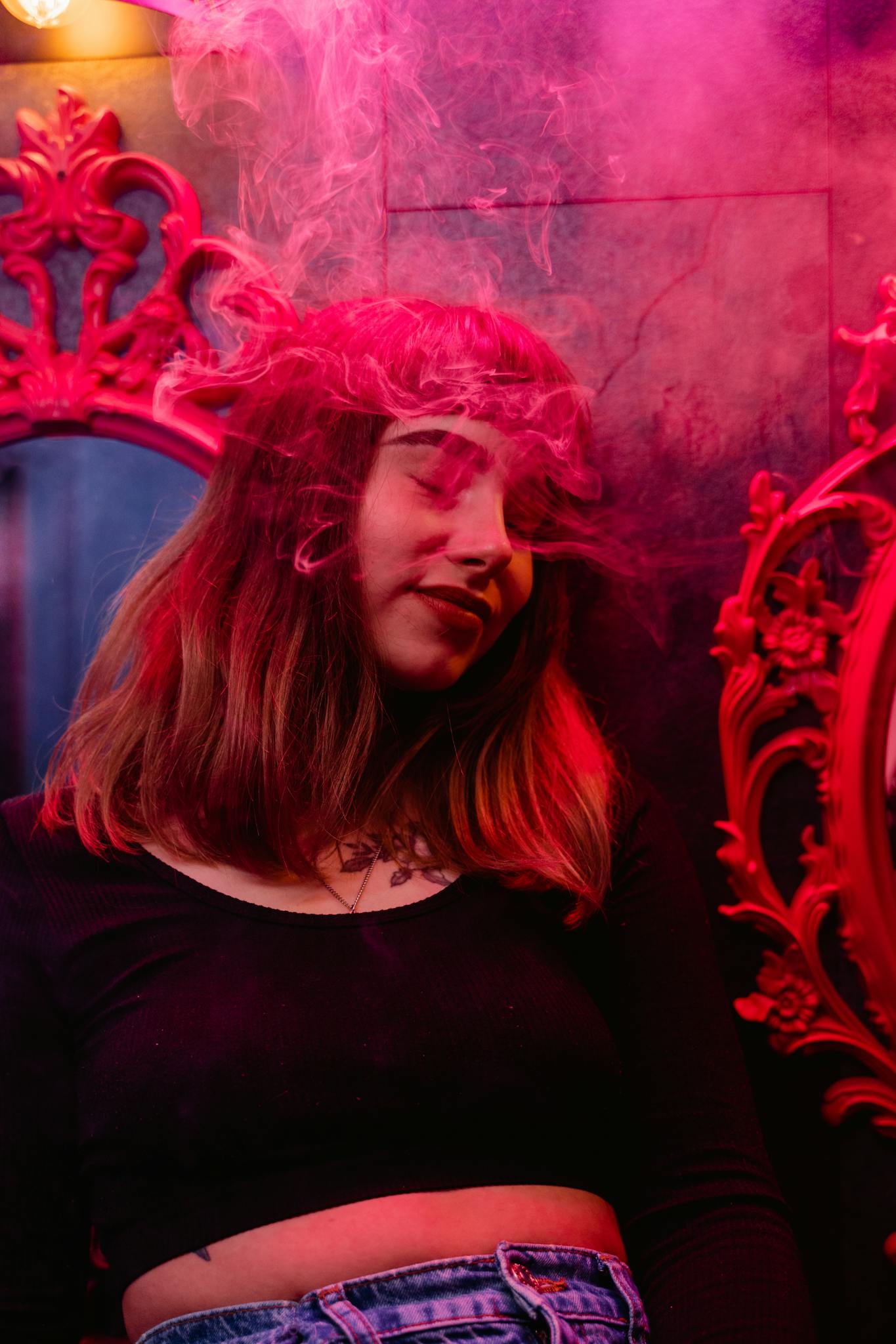 Stylish woman enjoying nightlife with colorful lighting and smoke effects.