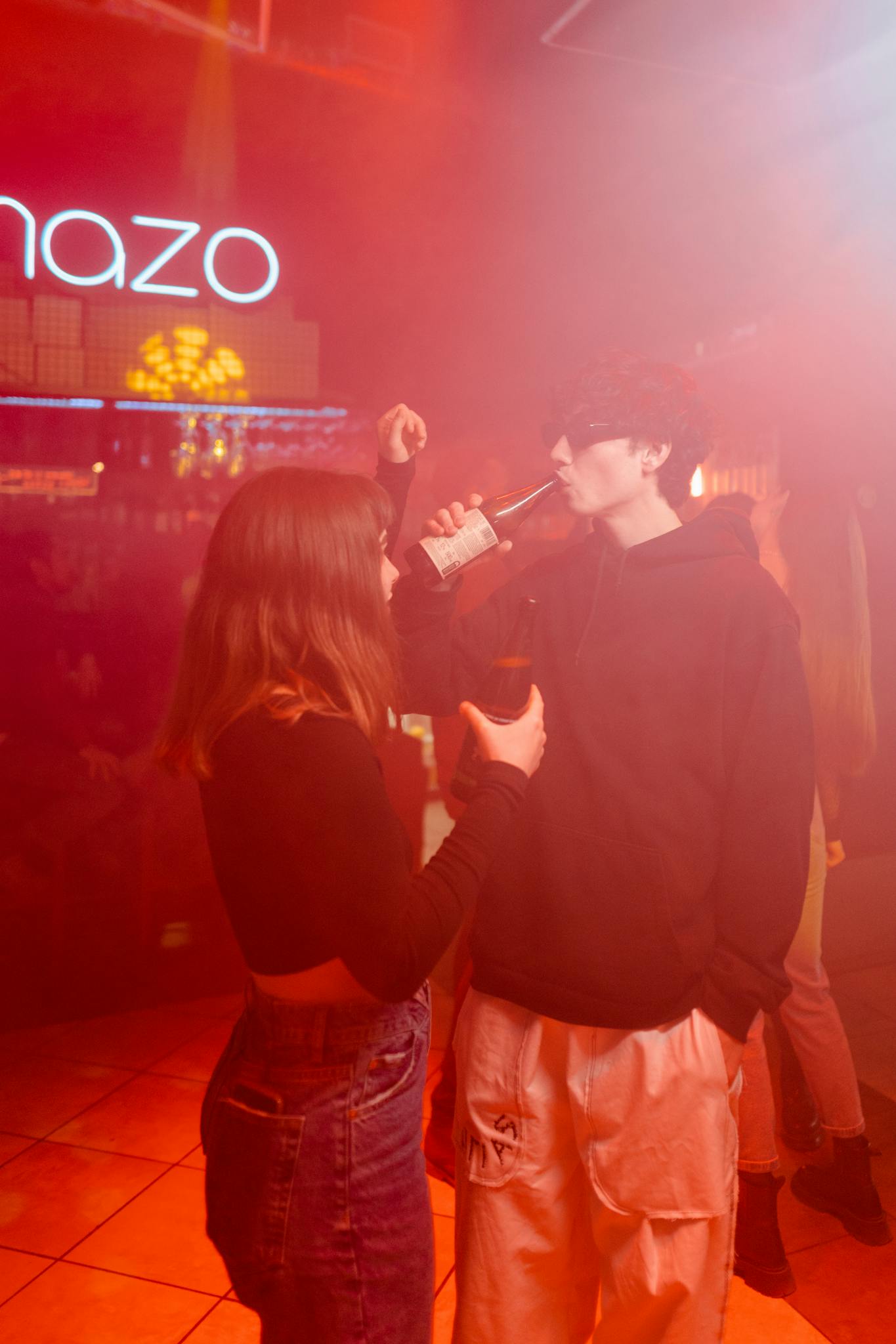 Two young adults enjoying drinks and music in a vibrant nightclub setting with red lighting.